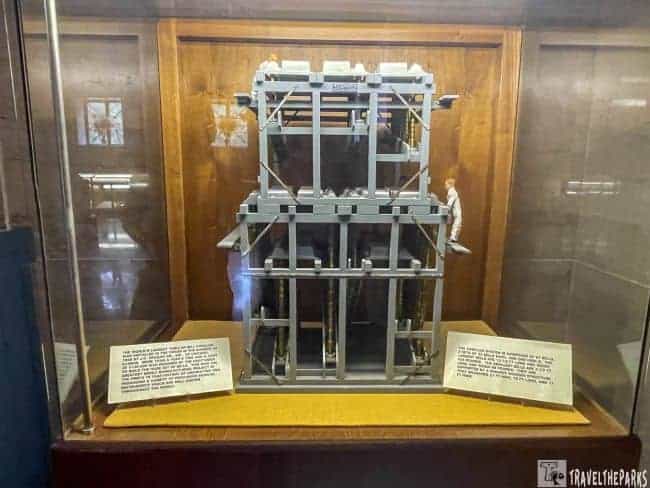 Model of a carillon bell structure in a glass display case with informational plaques in the Stephen Foster Folk Culture Center Museum.