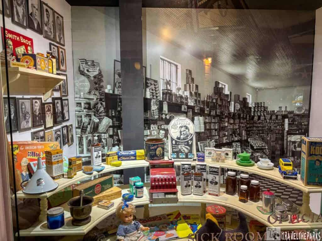 A museum exhibit of vintage pharmacy products with shelves full of colorful bottles and boxes, and a backdrop of a black and white photo of an old pharmacy.