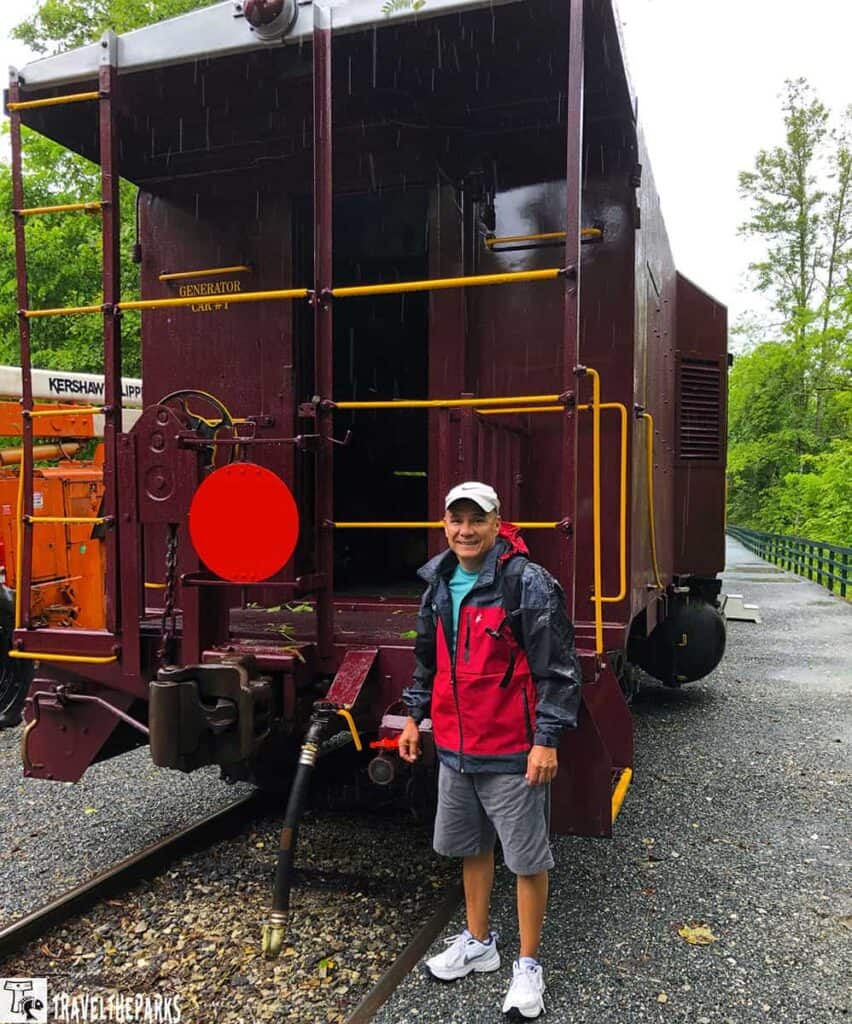 Person standing next to a maroon railway maintenance car in the rain.