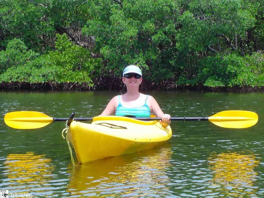 Person in a yellow kayak on calm water with green foliage in the background.