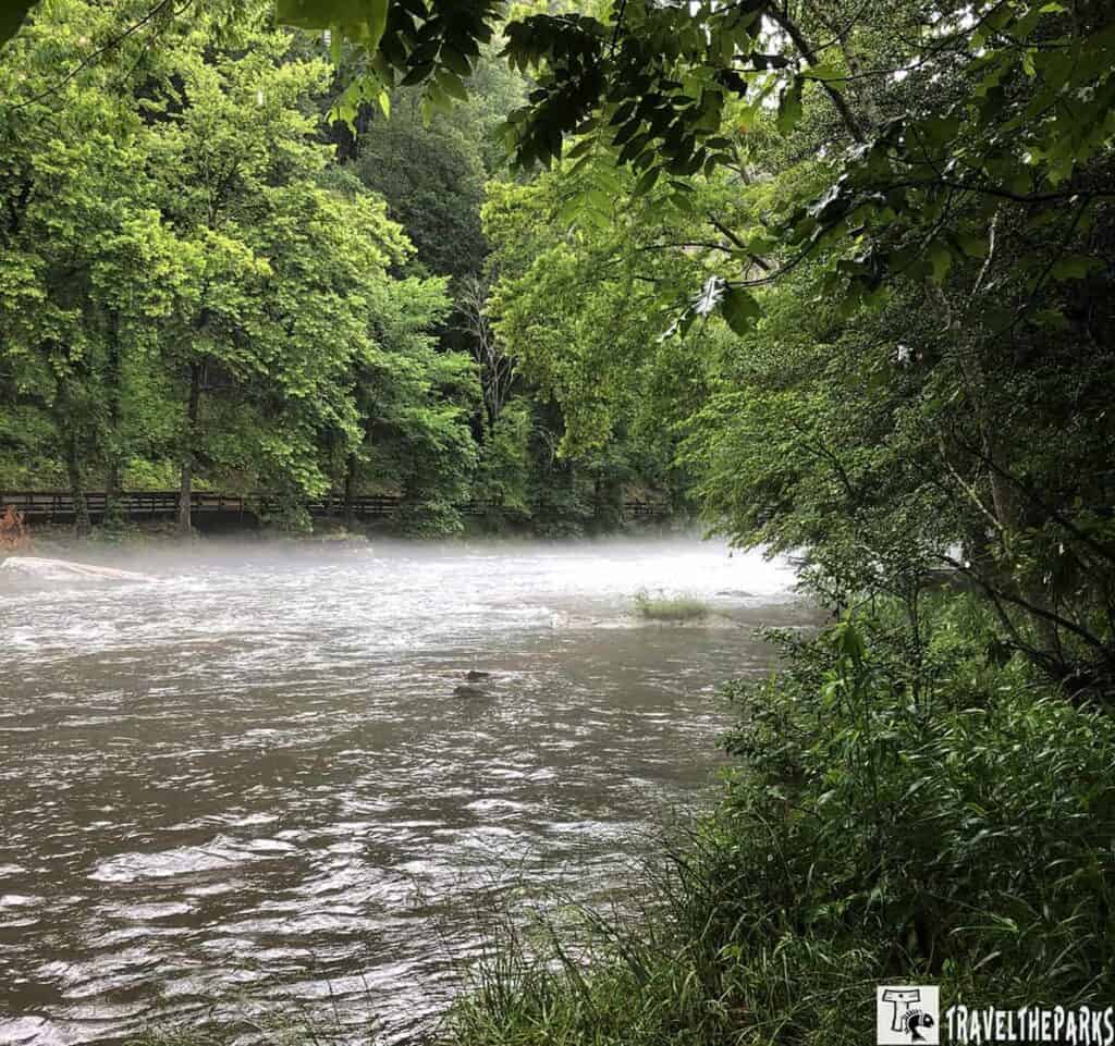 A misty Nantahala river flows through a dense green forest with a wooden fence in the background.