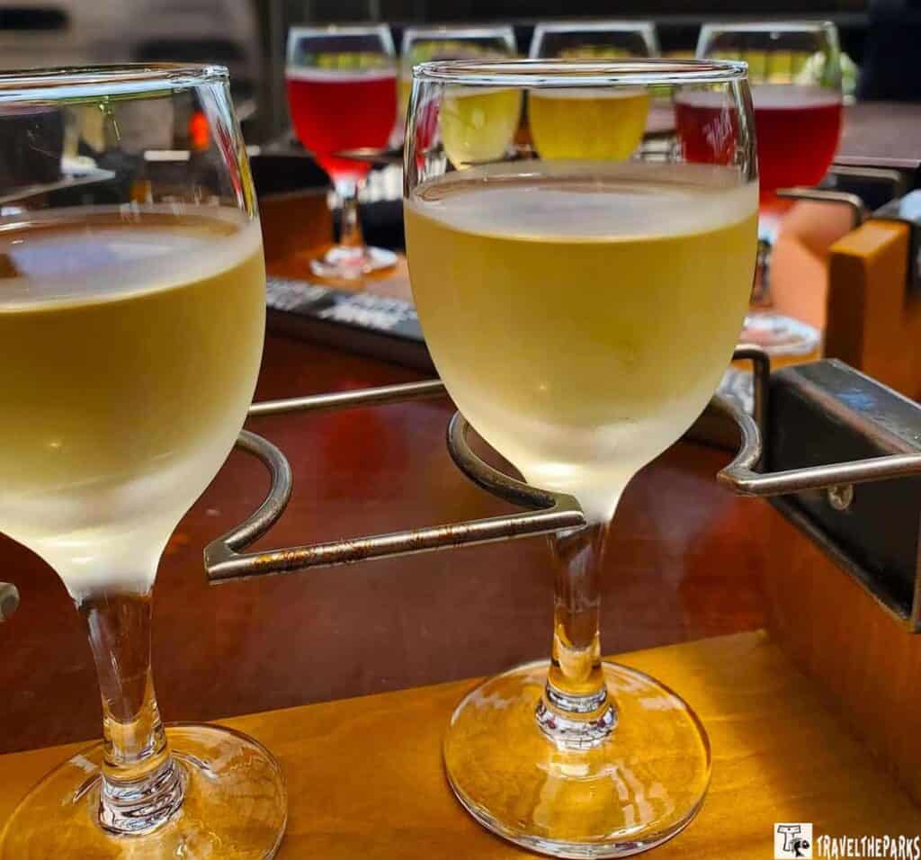 Close-up of a wine flight with glasses filled with white and red liquids on a wooden tray.
