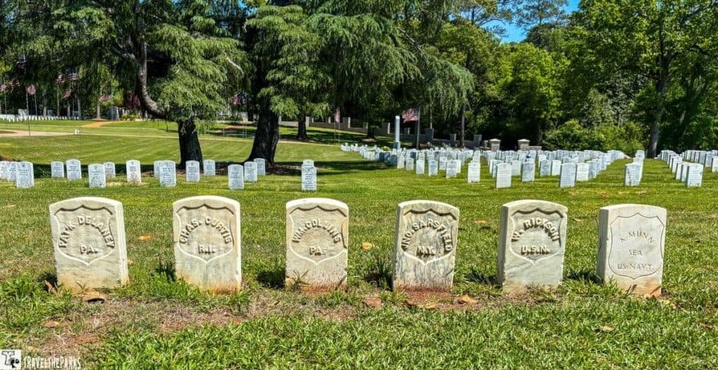 The Raiders 6 Headstones at Andersonville National Cemetery with trees and flags in the background.