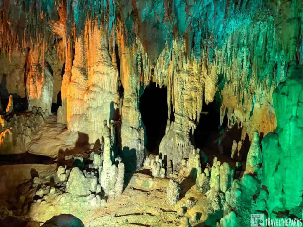 A brightly lit Cathedral Room interior with orange and green stalactites and stalagmites.