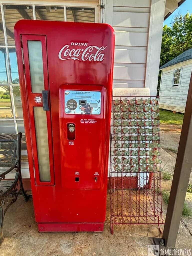 A vintage red Coca-Cola vending machine next to a rack of glass bottles.