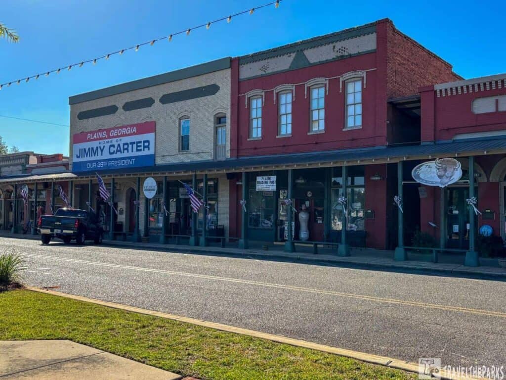 Street view of historic buildings in Plains, Georgia, with a sign about Jimmy Carter and American flags displayed.