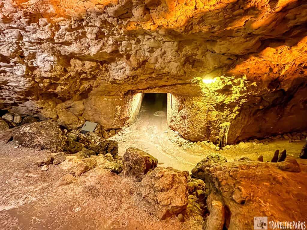 Interior of a rocky cave with a tunnel pathway illuminated by warm yellow-orange light.