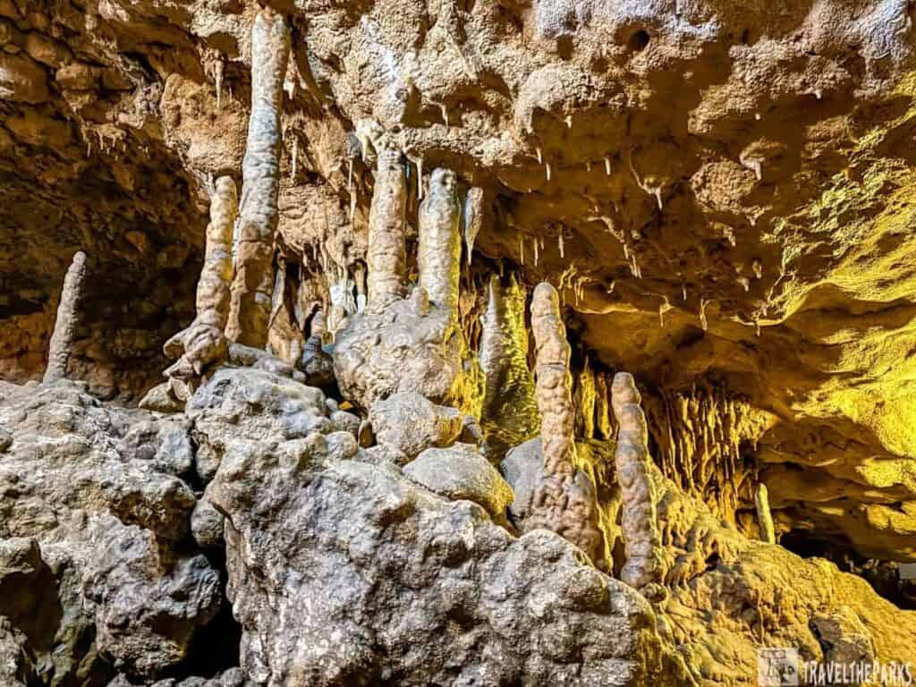 Cave interior with stalagmites and stalactites under warm lighting.