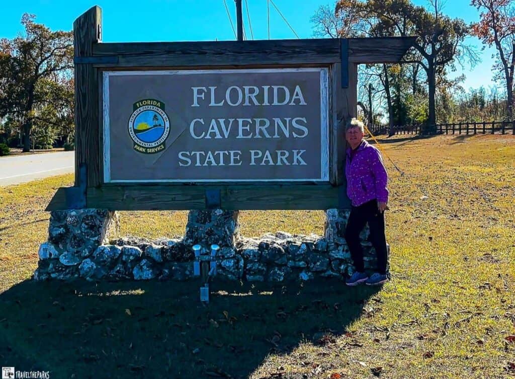 Sign for Florida Caverns State Park with a person standing beside it.