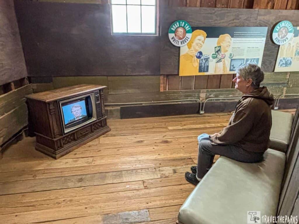 Person watching a vintage TV in a room with informational panels and wooden decor.