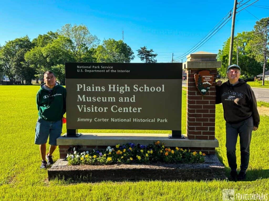 Two people stand next to a sign for the Plains High School Museum and Visitor Center at Jimmy Carter National Historic Park.