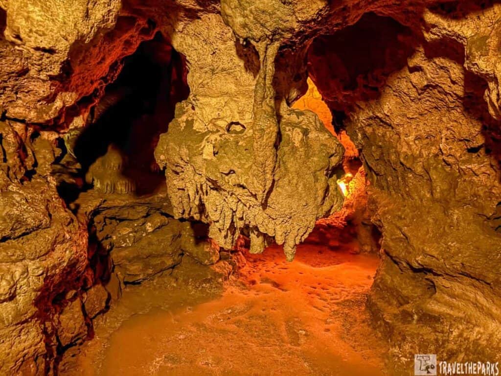 Cave interior with illuminated stalactites and stalagmites in warm amber light.