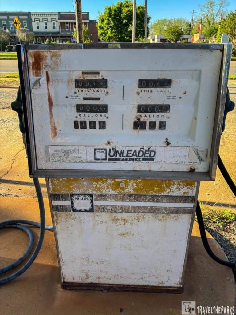 An old, rusted gasoline pump with faded labels and Phillips 66 logo on a concrete surface, set against a street backdrop.