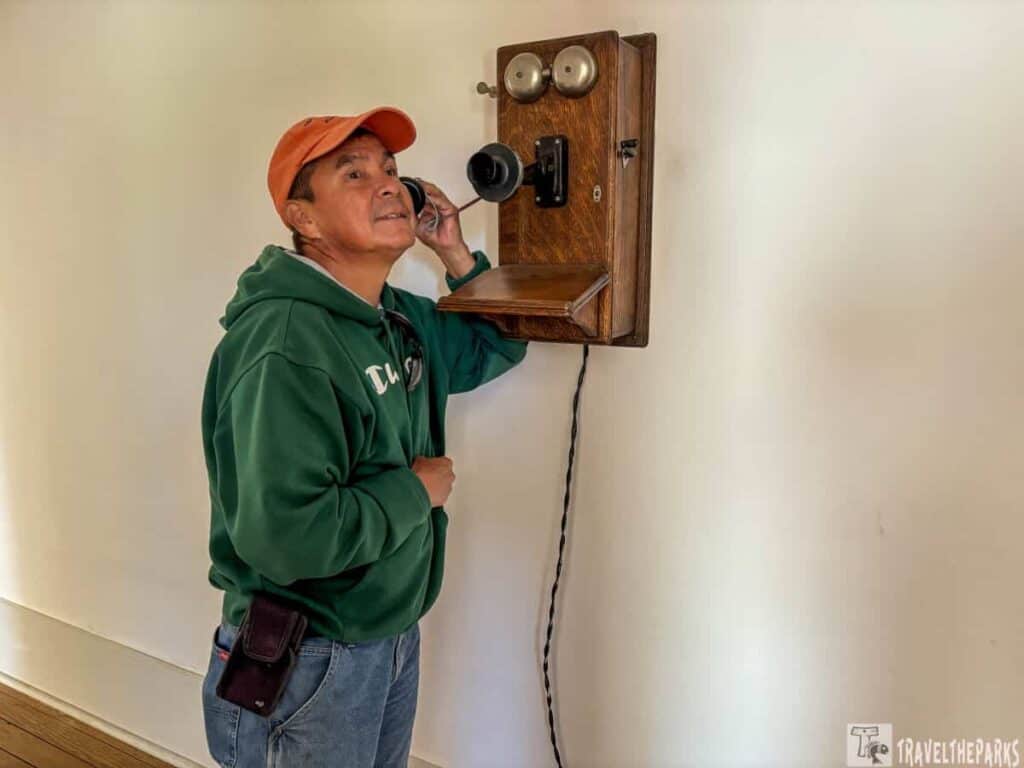 A person in a green hoodie using a vintage wooden wall-mounted telephone.