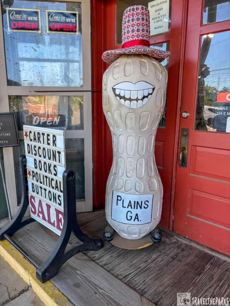 Storefront with a smiling peanut statue and a freestanding sale sign.