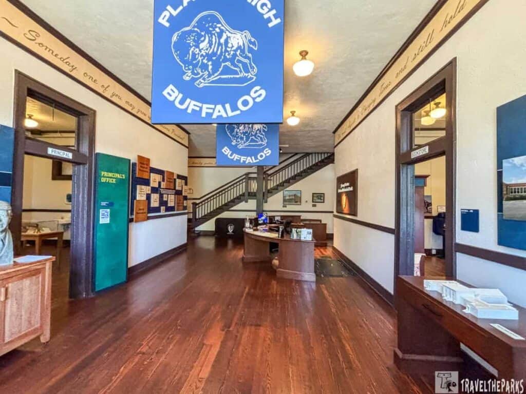 Interior of a school hallway with banners labeled "Plains High Buffalos," and signs for the principal's office and bookstore.