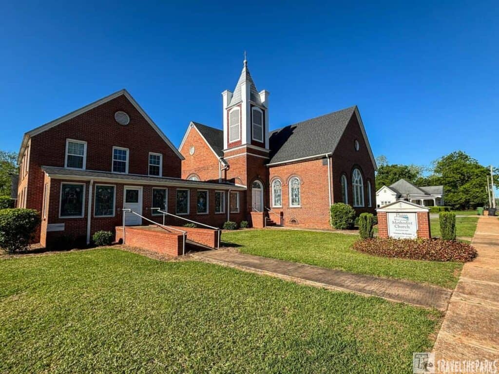 Red-brick church with a tower and stained-glass windows, under a blue sky.
