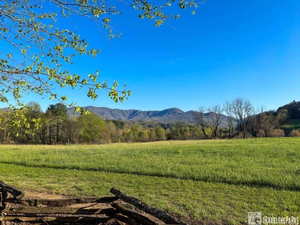 Scenic view of a grassy field, wooden fence, and distant mountains under a clear blue sky in the Great Smoky Mountains.