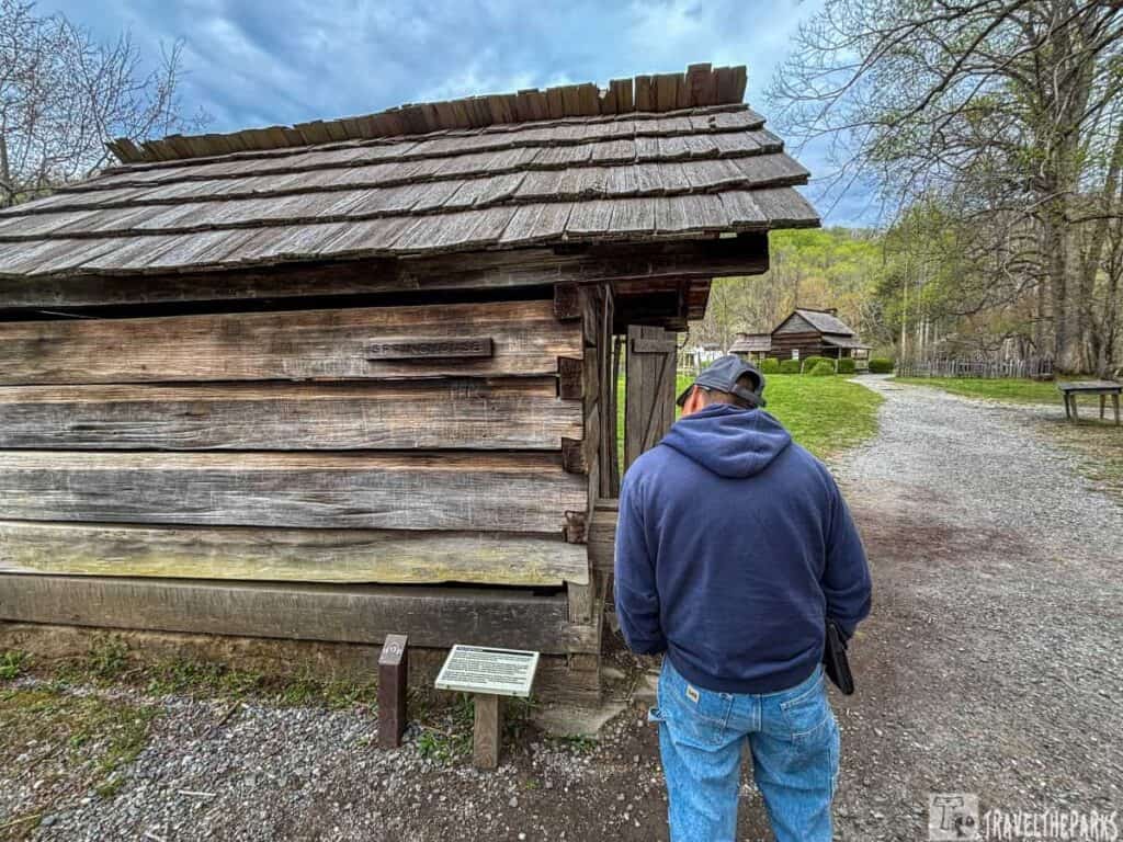 A person in a cap and hoodie stands by a wooden springhouse at the Oconaluftee Mountain Farm Museum.