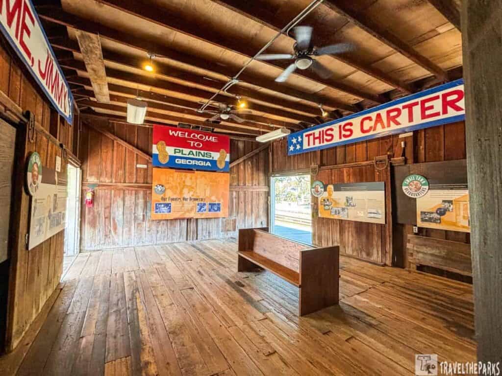 Interior of a wooden building with banners about Plains, Georgia, and Jimmy Carter election campaign signs.