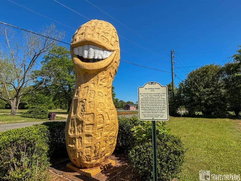 A large peanut sculpture with a smiling face stands outdoors alongside an informational sign.