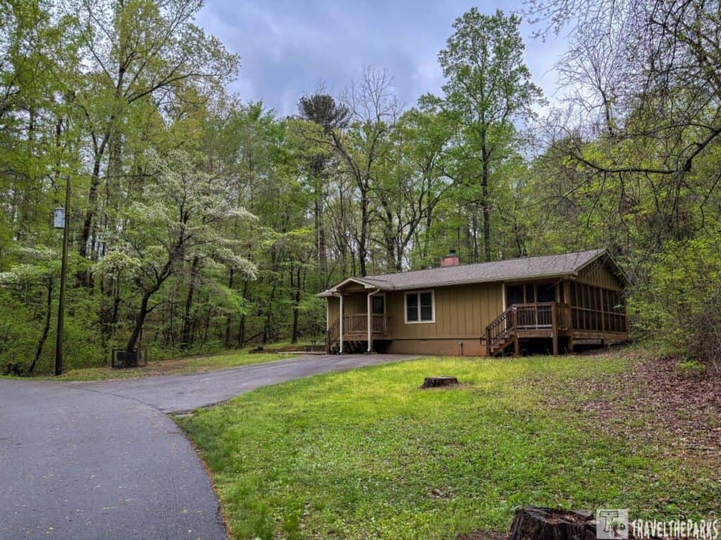 Cabin in a wooded area at Hard Labor Creek State Park with surrounding trees and a paved path.