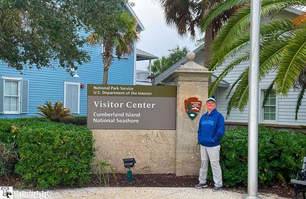 Visitor center sign for Cumberland Island National Seashore with a person standing next to it.