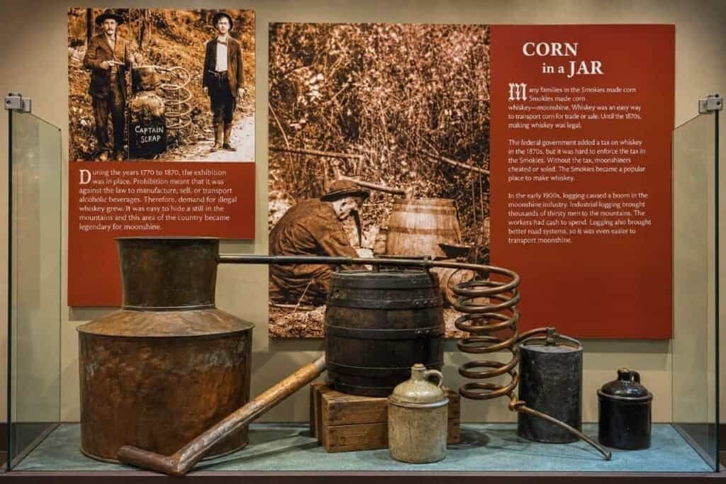 Oconaluftee Visitor Center: Museum exhibit displaying historical moonshining equipment with photographs and informational panels.