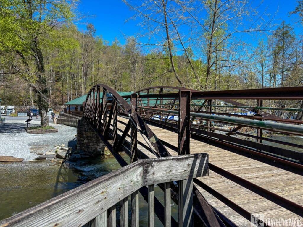 A wooden and metal bridge over the Nantahala river under a bright blue sky with trees nearby.