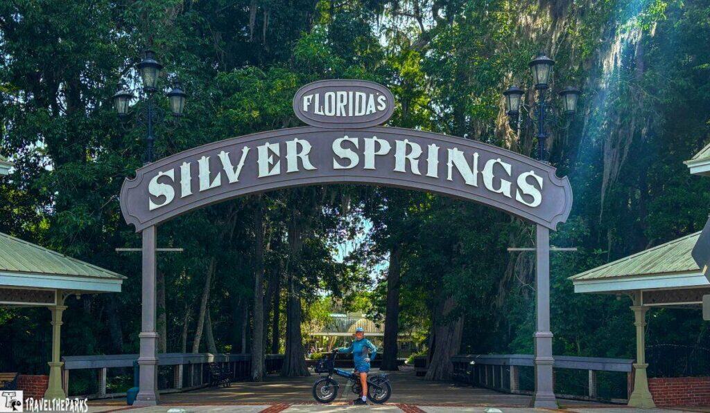 Entrance to Florida’s Silver Springs with a large arched sign and a person with a bicycle beneath it.