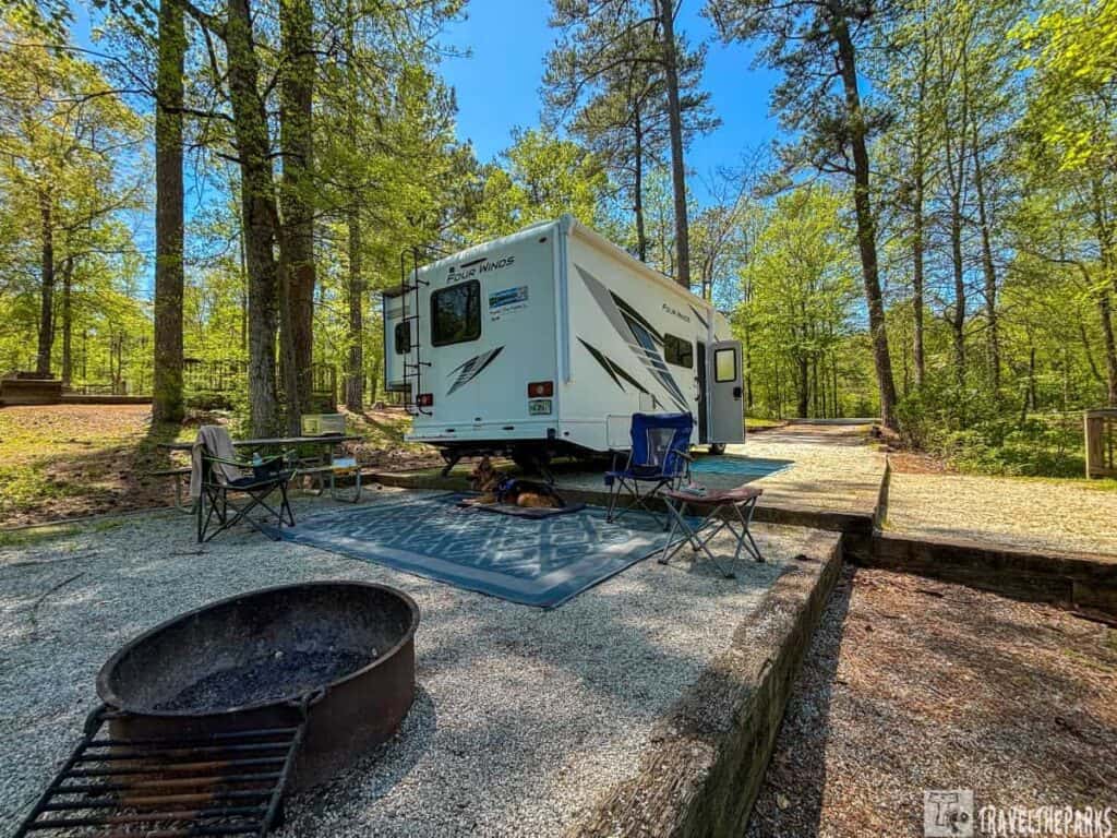 Campsite #37 at Hard Labor Creek State Park. A white recreational vehicle (RV) with a dog on a mat and campfire grill with lawn chairs around