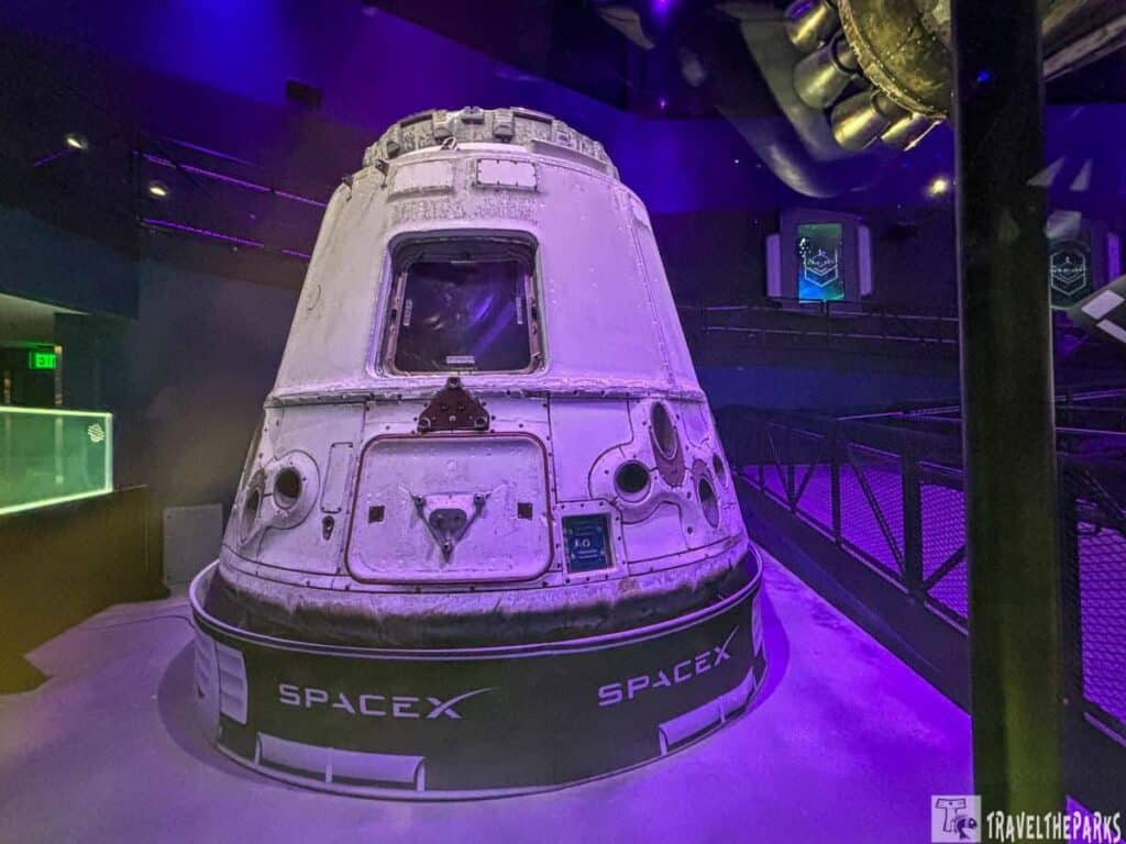 SpaceX capsule on display in a dimly lit exhibition with purple lighting.