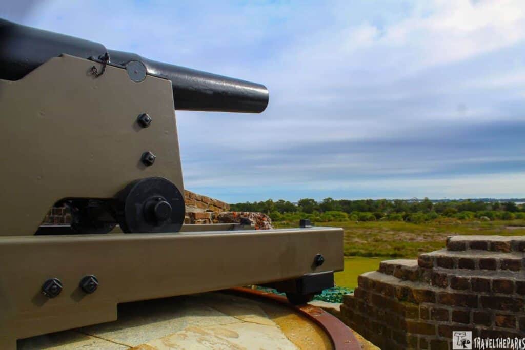 A historic cannon on a brick fortification against a cloudy sky and distant landscape.