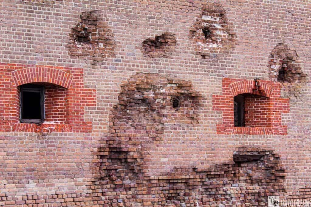 Damaged brick wall of Fort Pulaski with impact marks and two window openings.