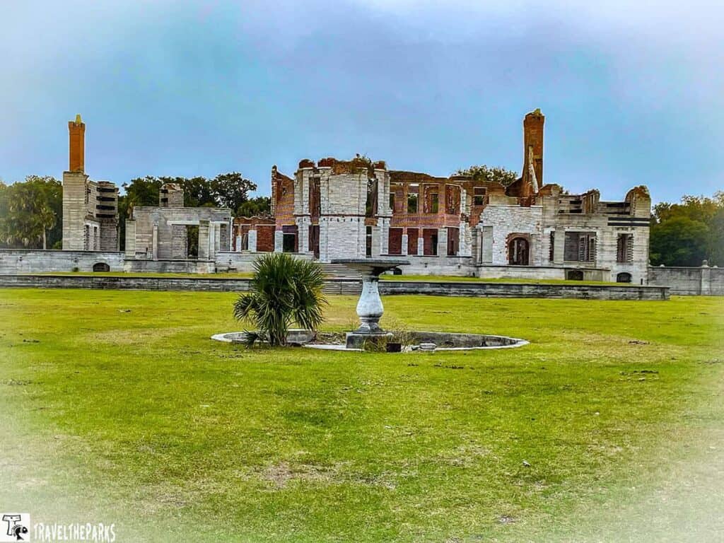 Dungeness Ruins on Cumberland Island with crumbling stone and brick walls, chimneys, and a manicured lawn in the foreground.