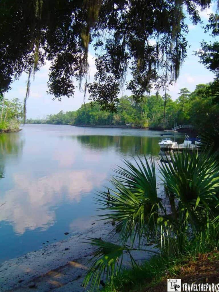 Tranquil river scene with reflecting water, greenery, and boats.
