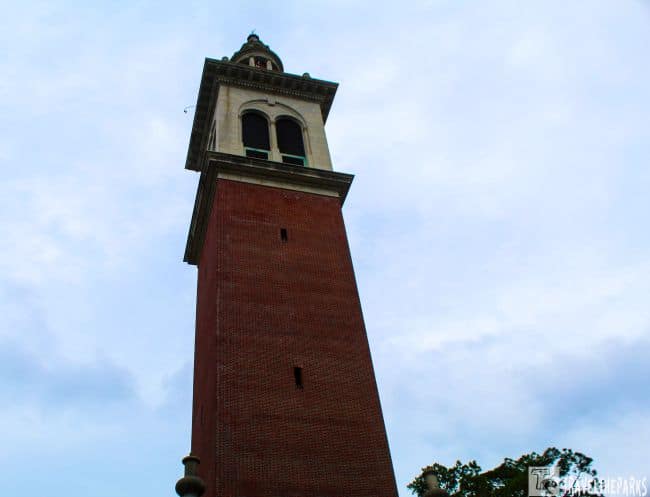 A tall brick tower with arched windows at the top against a cloudy sky.