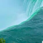 View of Niagara Falls with emerald green water cascading over the edge, creating mist.