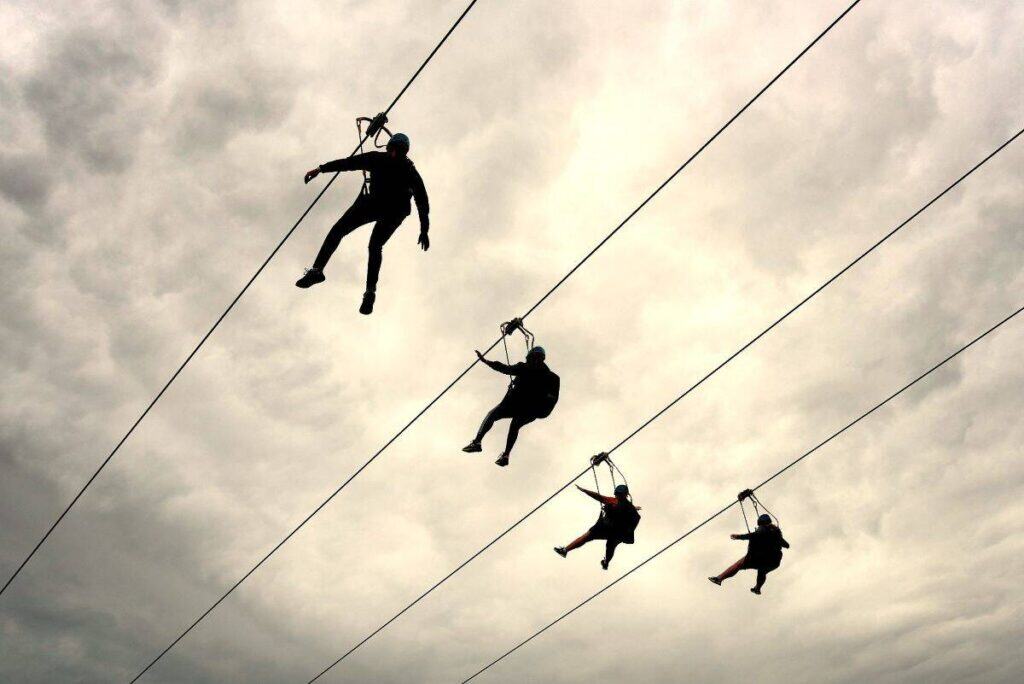 Four people ziplining against a cloudy sky.