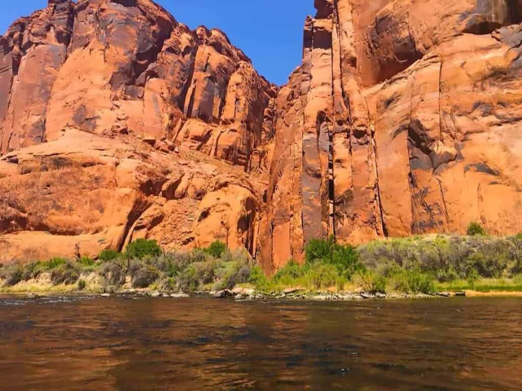 Towering red sandstone cliffs and the calm Colorado River in Glen Canyon.