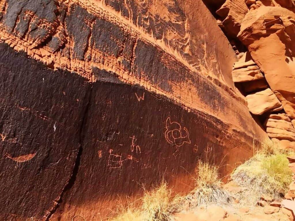 Canyon wall with petroglyphs and contrasting red and dark brown rock surface.