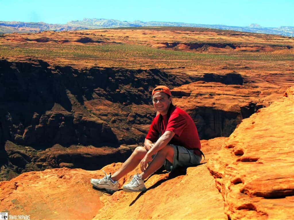 A person sits on a cliff edge at Horseshoe Bend with a vast desert landscape in the background.