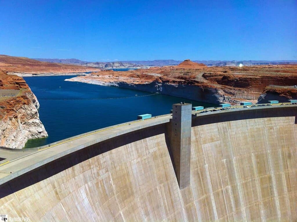 Aerial view of a large concrete dam in front of Lake Powell with red rock formations in Glen Canyon.