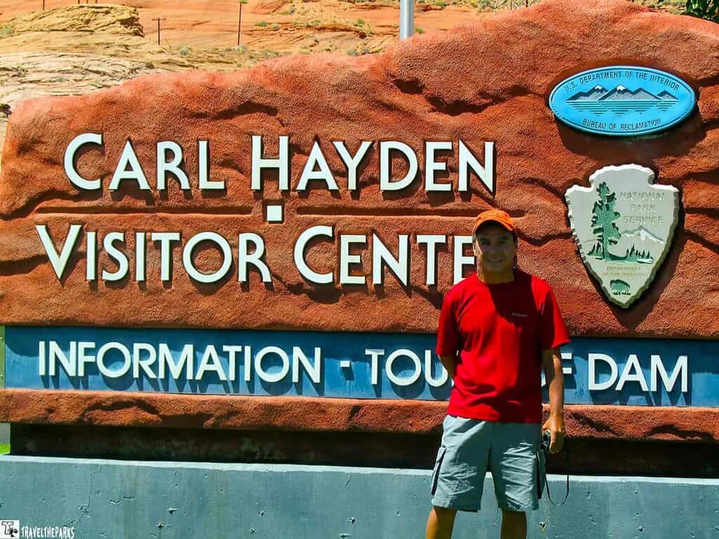 A person stands in front of the Carl Hayden Visitor Center sign made of red rock.