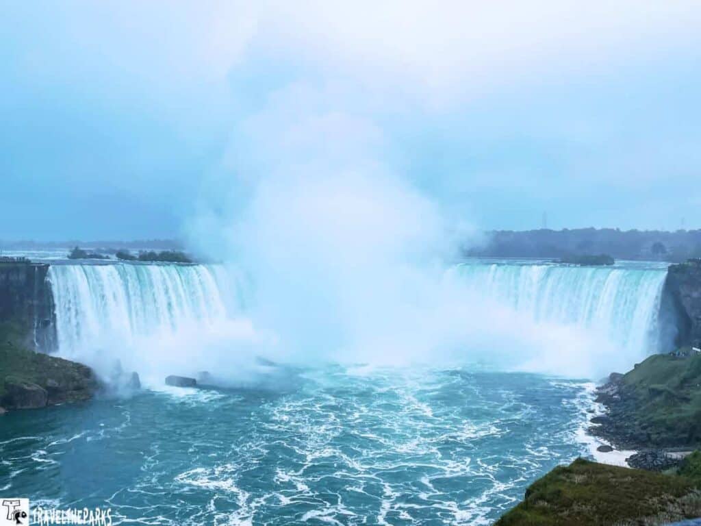 Niagara Falls with water cascading over the Horseshoe Falls, creating mist and turbulent water below.