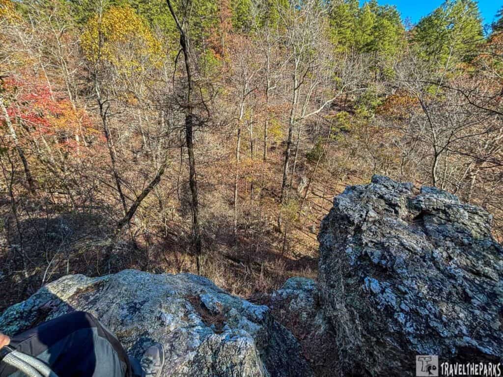 View from a rocky outcrop overlooking an autumn forest with visible hiker's leg and boot.