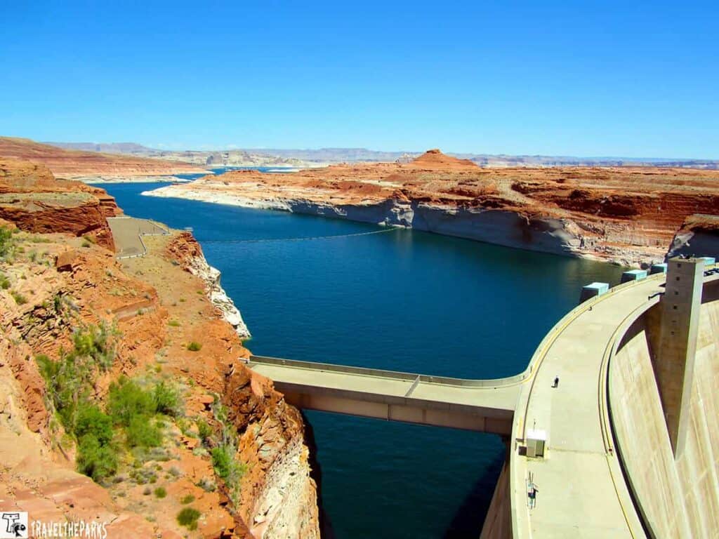 View of Glen Canyon Dam and Lake Powell with red rock cliffs and blue sky.