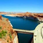 View of Glen Canyon Dam and Lake Powell with red rock cliffs and blue sky.