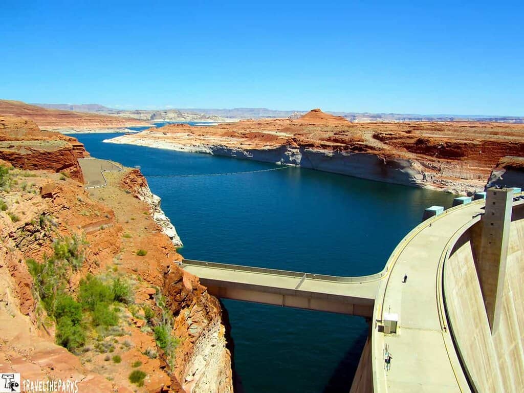 View of Glen Canyon Dam and Lake Powell with red rock cliffs and blue sky.