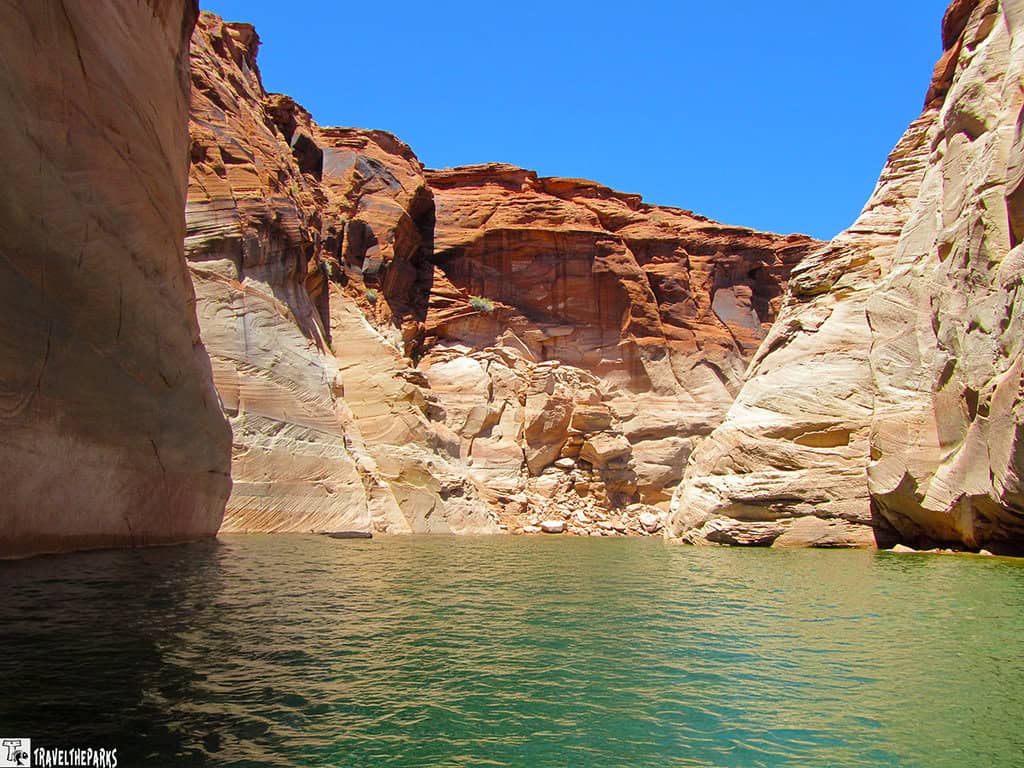 Steep sandstone cliffs surrounding greenish-blue water at Lake Powell under a clear blue sky.